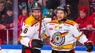 Niklas Olausson till vänster och Einar Emanuelsson till höger ler och firar ett mål med ryggen mot sargen.