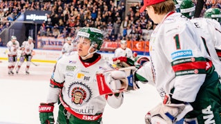 Frölundaspelare i vit tröja gör high five med målvakt på avbytarbänken. I bakgrunden ses ytterligare Frölunda-spelare och Växjöpublik